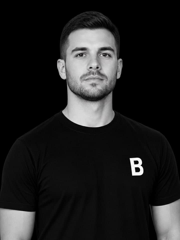 A coach in a black team shirt, photographed against a dark background.