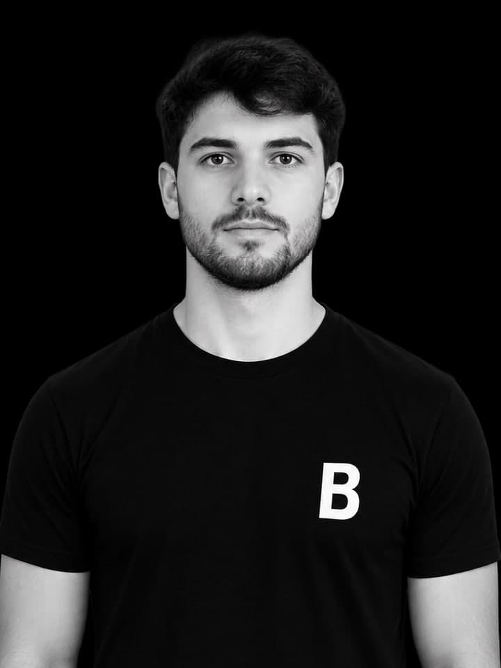 A second coach in the same black team shirt, photographed against a dark background.
